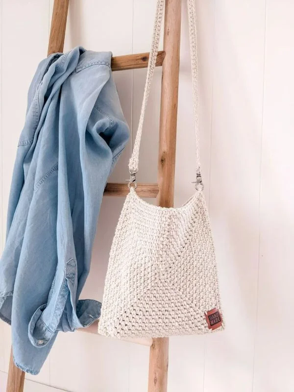 A white granny square crossbody bag hanging off a wooden ladder.