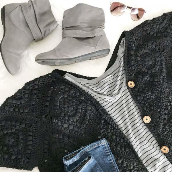 A flat lay of a black crochet grannu square cardigan with grey boots,  jeans, and a striped tee.
