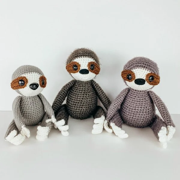 Three crochet sloths sitting in a row.