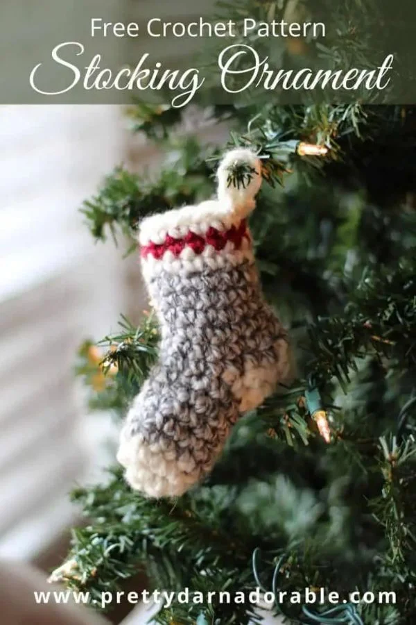 A miniature crochet Chritmas stocking hanging on a Christmas tree.