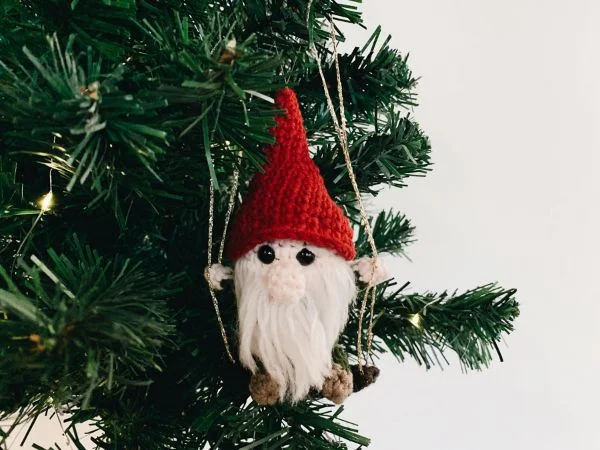A crochet gnome on a swing hanging from a Christmas tree.
