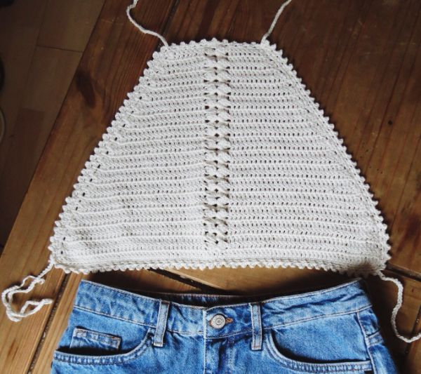 A flat lay image of a white crochet halter top with tie straps.