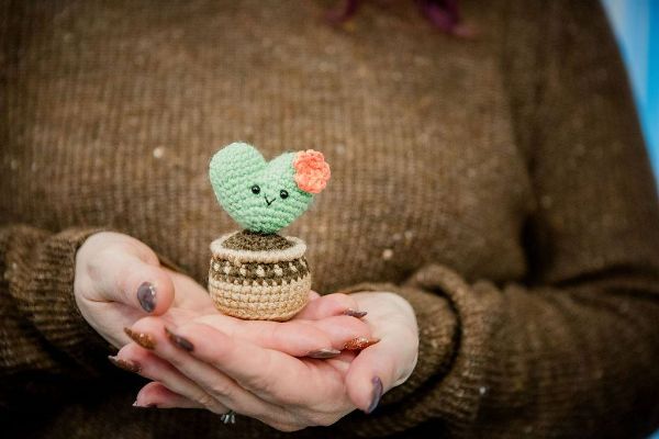 A person holding a little heart-shaped crochet cactus.