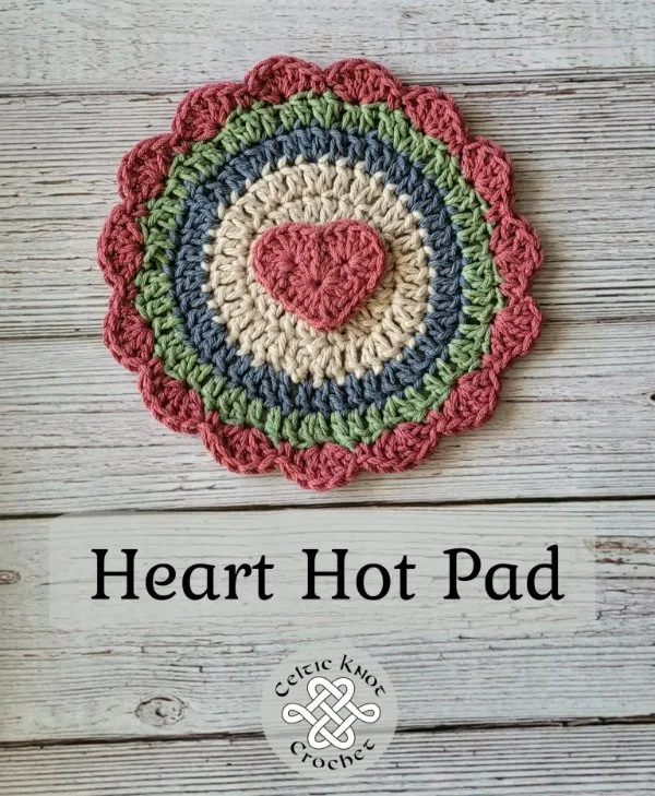 A coloured round crochet trivet with a heart motif.