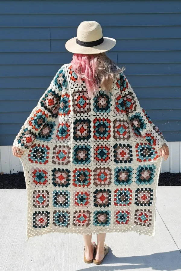 Back view of a woman wearing a long granny square cardigan with a hat.