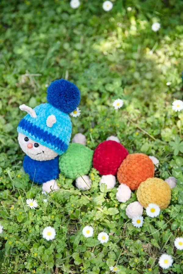 A rainbow-coloured crochet caterpilar wearing a beanie.