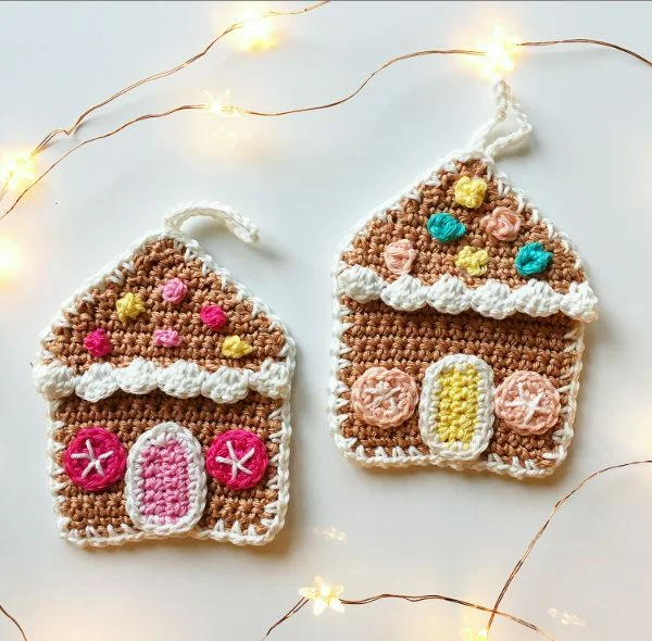 Two small gingerbread house crochet Christmas ornaments in pretty pastel colours.