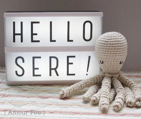 A beige crochet octopus sitting in front of a light box.