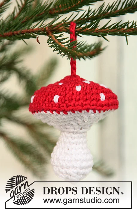 A crochet mushroom ornament with a red cap and white spots hanging from a Christmas tree.