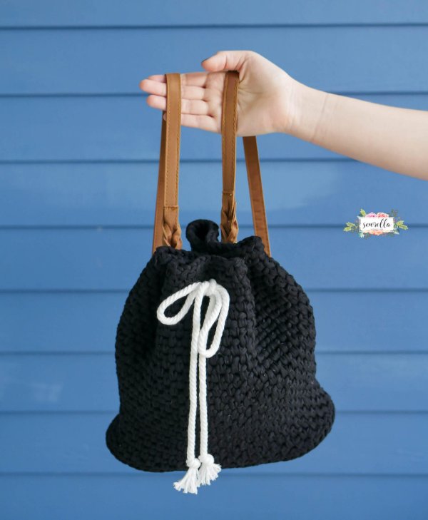A black crochet backpack with a white drawstring and brown leather straps.