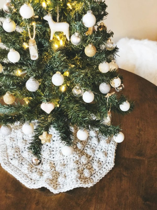 A closeup of a tabletop Christmas tree with a mini crochet Christmas tree skirt.