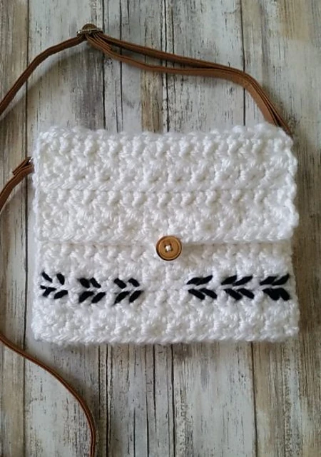 A small white crochet bag with a wooden button and smple black arrow embroidery detail.
