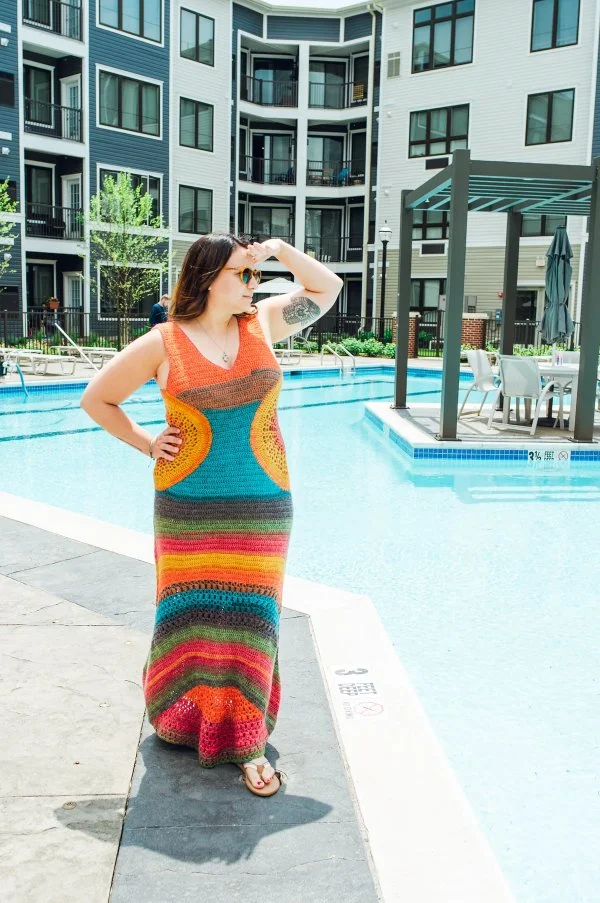 A woman by a pool wearing a brightly coloured crochet maxi dress