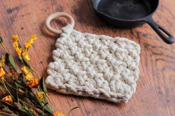 A chunky textured crochet trivet with a wooden loop.