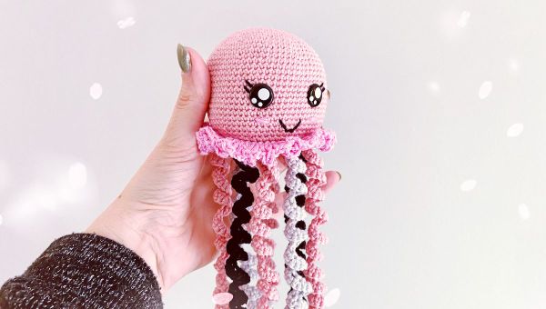 A pink, white, and black crochet octopus with a cute facial expression.