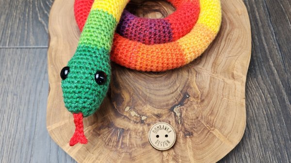 A crocheted rainbow snake on a wooden board.