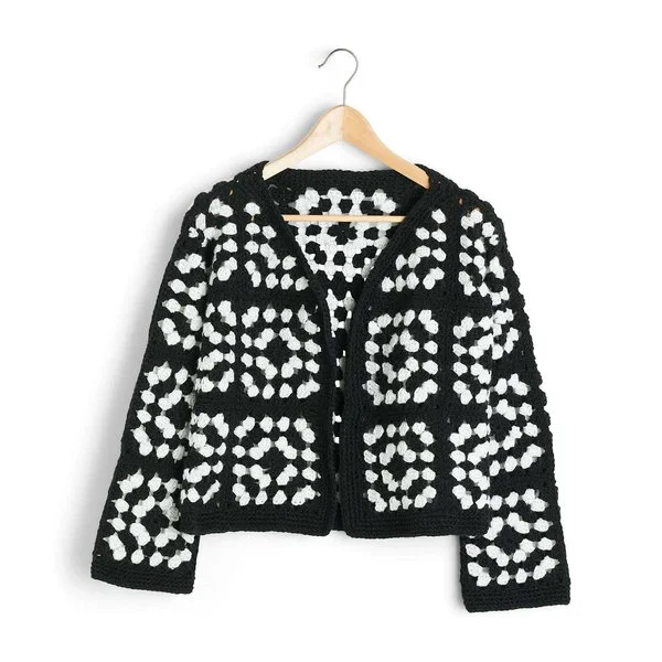 A cropped length, black and white crochet Granny Square cardigan on a wooden hanger.