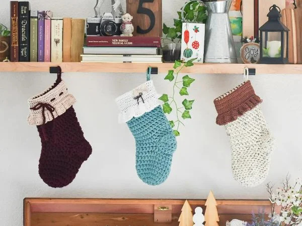 Three crochet Christmas stockings in different colours haning over a mantle.