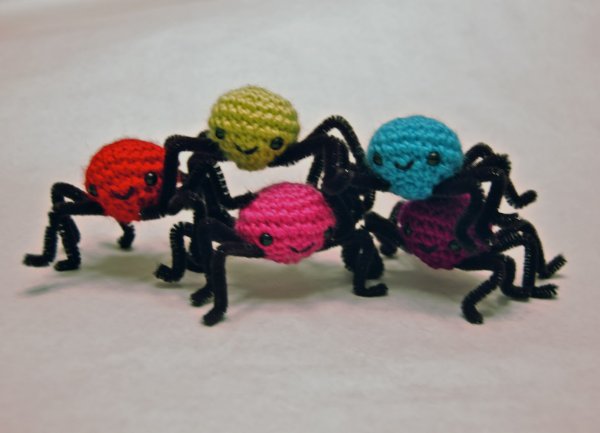 Five different coloured crochet spiders stacked on top of each other.