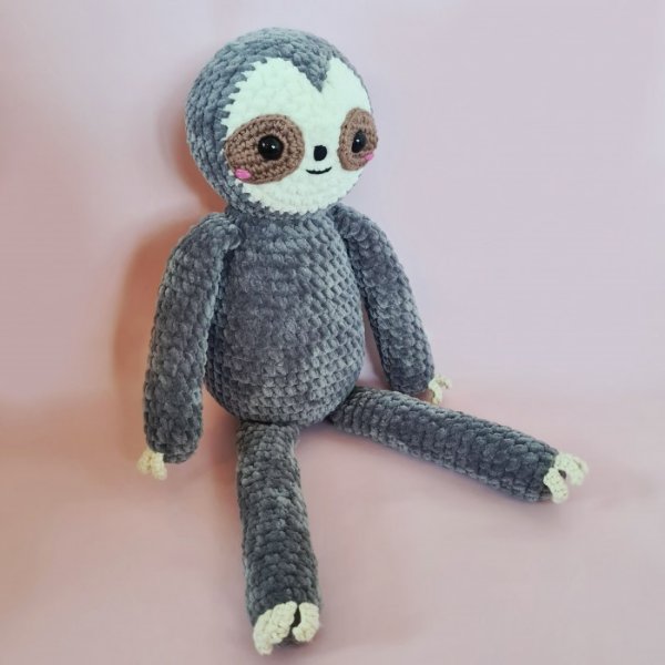 A grey crochet sloth toy on a pink background.