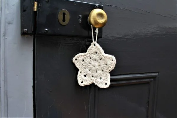 A white crochet Christmas star ornamnet hanging from a black door.