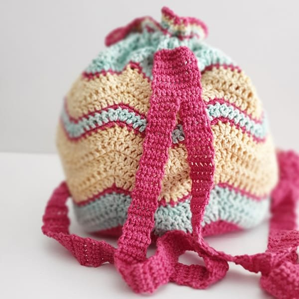 Cheveron striped crochet backpack with pink straps and pompoms.