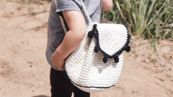 A child wering a white crochet backpack with black details.