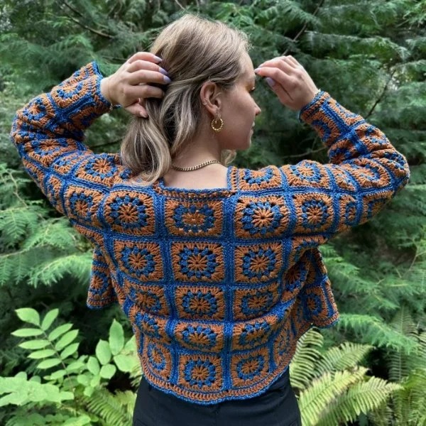Back view of a woman wearing a blue and orange crochet granny square cardigan.