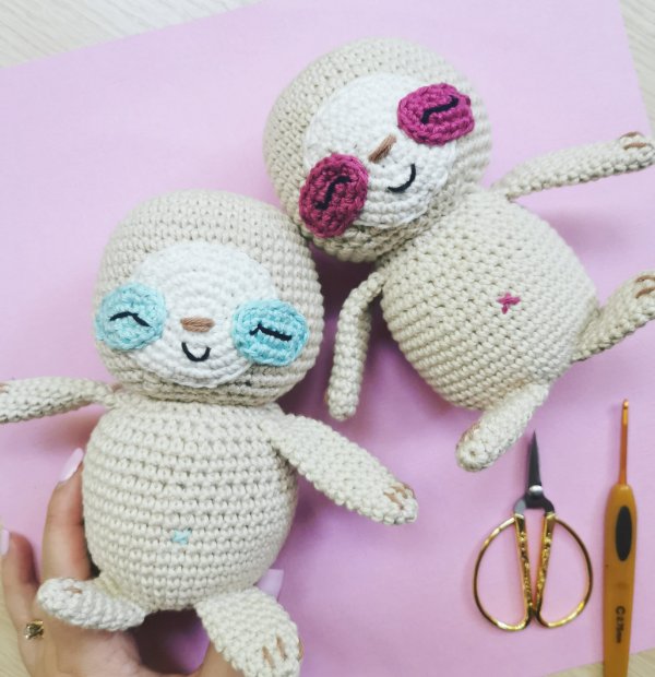 Two crochet sloths with coloured eye patches.
