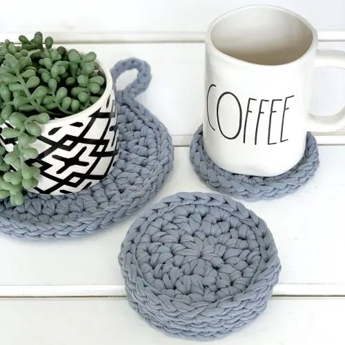 A set of grey blue crochet coasters with coffee and a small pot plant.
