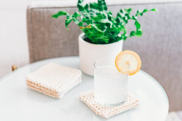 A set of light coloured crochet coaster on a table with a cocktail.
