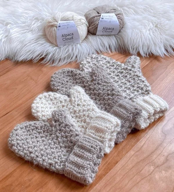Four different sizes and coloured crochet mittens in a row,