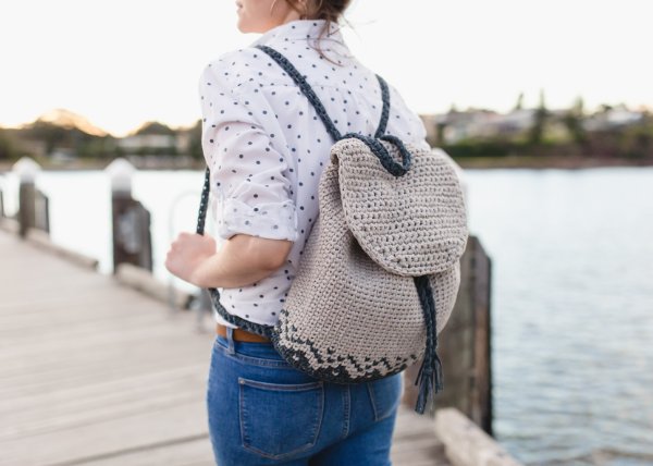 A woman on a pier, wearing a crochet backpack with tapestry crochet details.