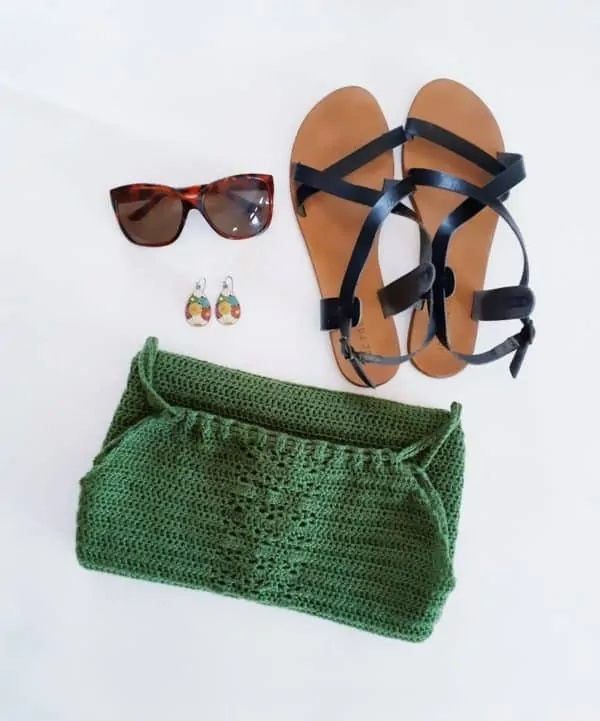 A flatlay image of a green crochet halterneck top, sandals, and sunglasses.