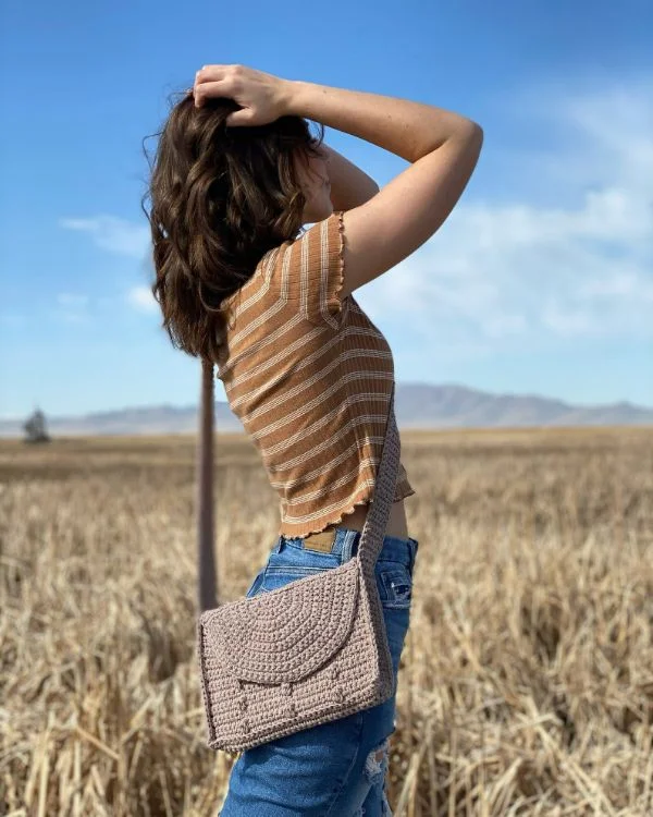 A woman outdoors wearing a crochet crossbody bag with bobble stitch detail.