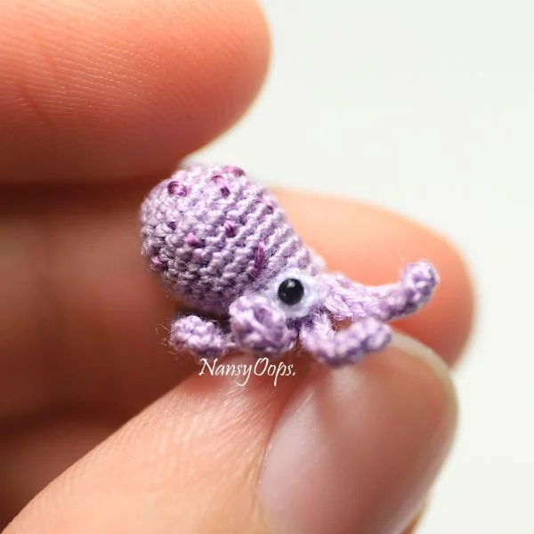 A tiny crochet octopus sitting on a fingertip.