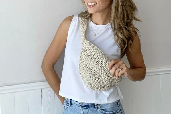 A woman wearing a natural coloured crochet crossbody bag with a crochet strap.