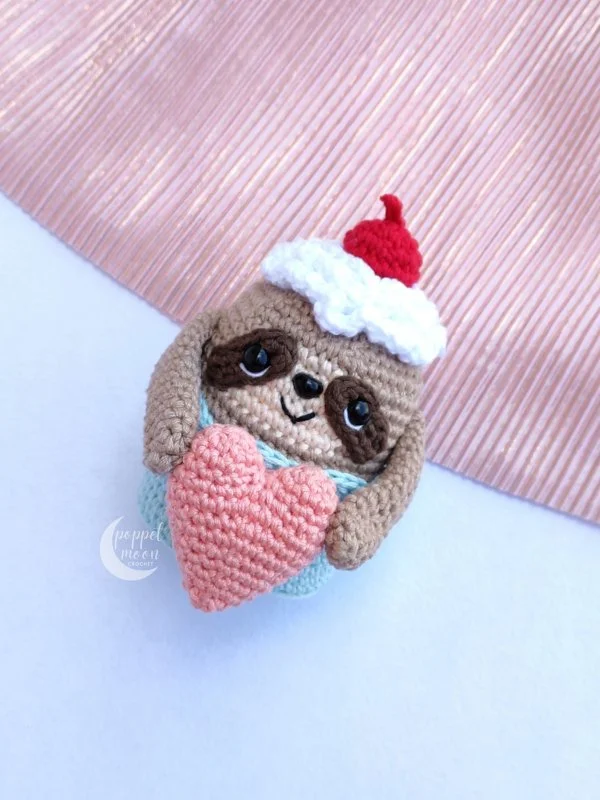 A valentines day themed crochet sloth holding a love heart.