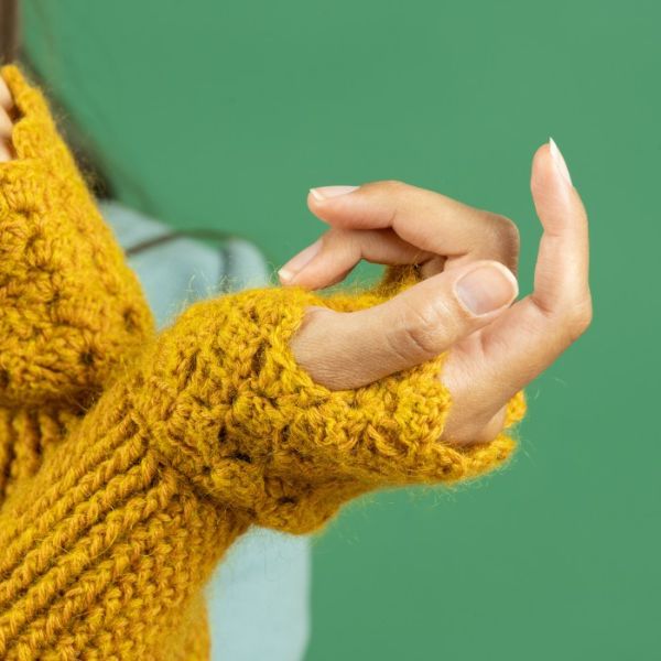 A close up of a womans hanbds wearing mustard yellow crochet wrist warmers.