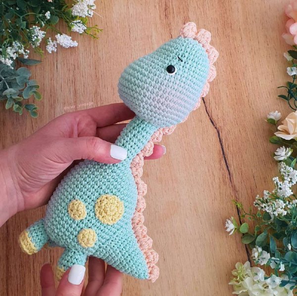 Someone holding a cute amigurumi dinosaur made in soft pastel colours.