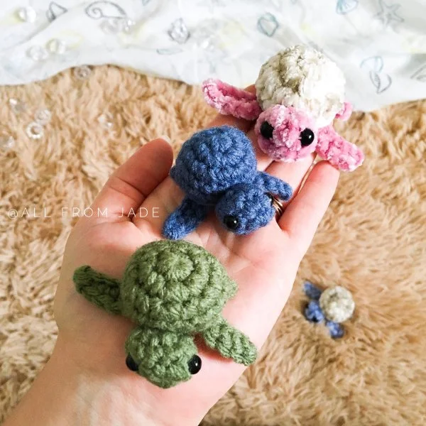 Three different coloured crochet baby turtles held in the palm of a hand.