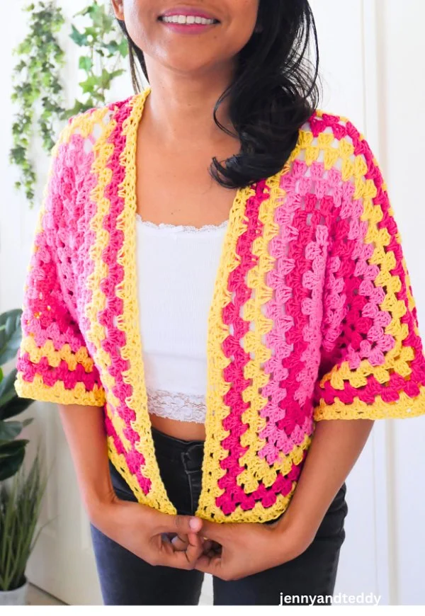 A woman wearing a brightly coloured crochet hexagon cardigan with short sleeves.