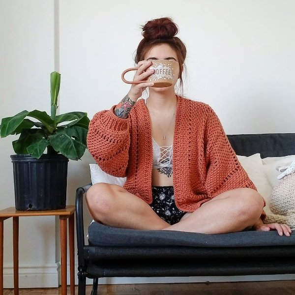 A woman sitting cross-legged on a sofa wearing a hexagon crochet cardgian.