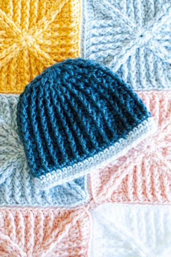 A textured stitch crochet baby hat sitting on a crochet baby blanket.