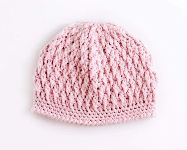 A pink crochet baby beanie featuring textured front post stitches.