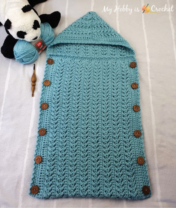 A hooded crochet baby cocoon with wooden buttons.
