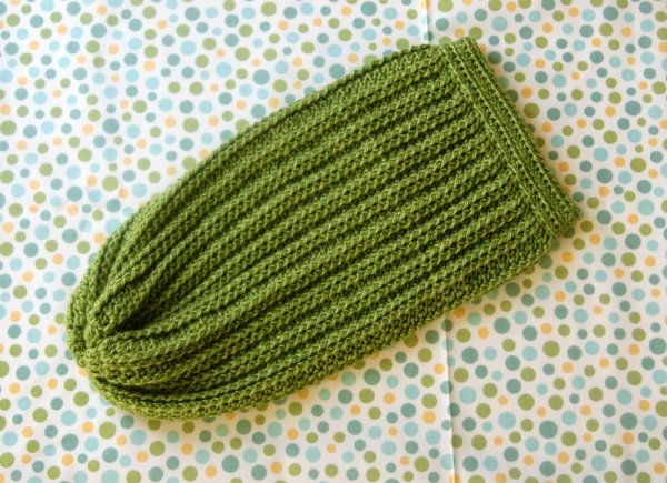 A flat lay image of a green crochet baby cocoon on a polka dot background.