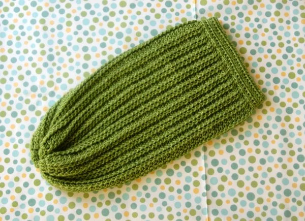A flat lay image of a green crochet baby cocoon on a polka dot background.