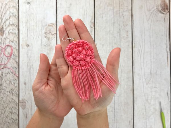 A woman holding a pink crochet earring in her hand.