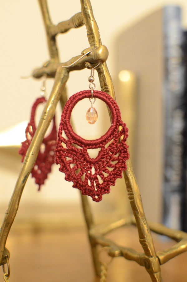 Prretty red crochet earrings hanging on a jewellery stand.